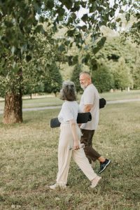 Pareja caminando en un parque con tapetes de yoga enrollados en los brazos.
